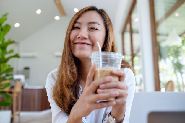 Portrait image of a beautiful young asian woman holding and drinking iced coffee in cafe