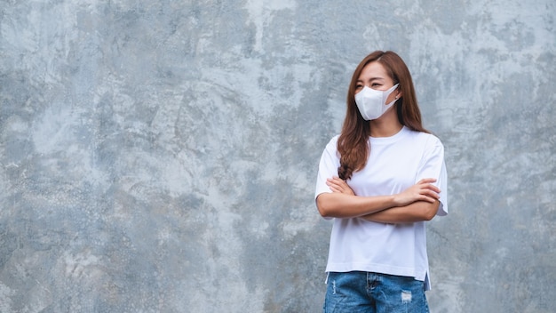 Portrait image of a woman wearing protective face mask standing in front of concrete wall background for Health care and Covid19 concept