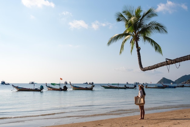 Portrait image of a woman with hat and bag strolling on the beach