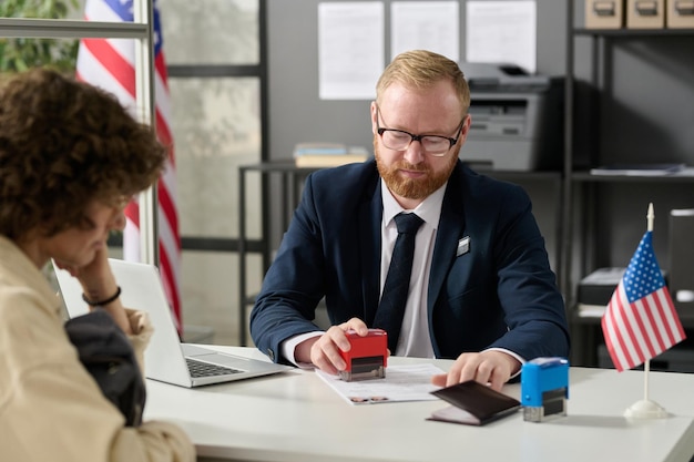 Portrait of immigration office worker stamping application form while working with client in cubicle