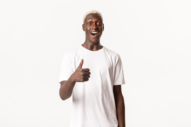 Portrait of impressed smiling african-american blond man, showing thumbs-up, praising good choice, making compliment