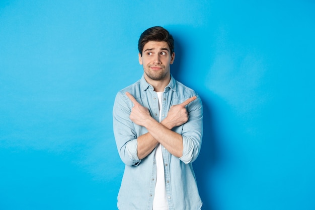 Portrait of indecisive adult man pointing fingers sideways but looking left