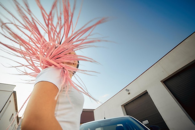 Portrait of an independent girl with pink pigtails on the background of the sky and the car the concept of modern society