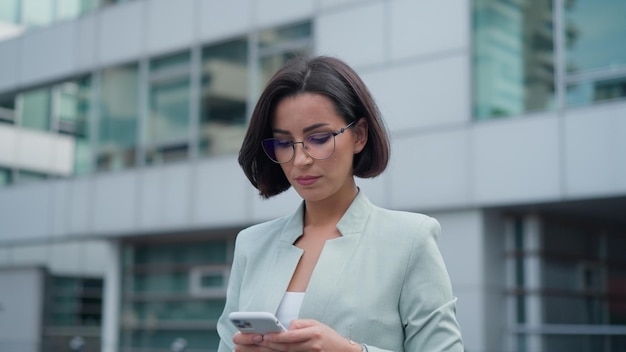 Portrait of independent proud woman with smartphone in her hands walking and answering business emails on an urban background