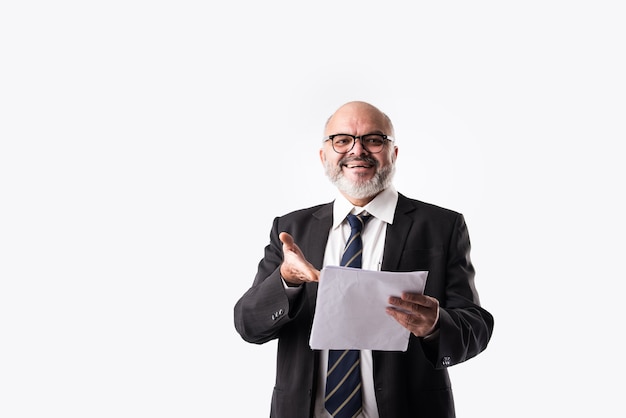 Portrait of Indian asian senior businessman holding or reading paper documents while standing against white background