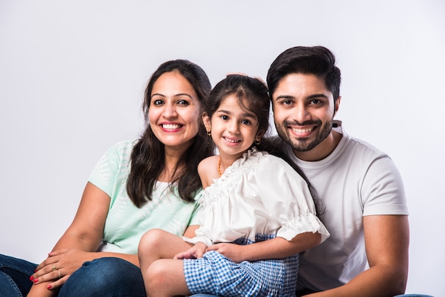 Portrait of Indian Asian young family of four sitting on white flour against white background, looking at camera