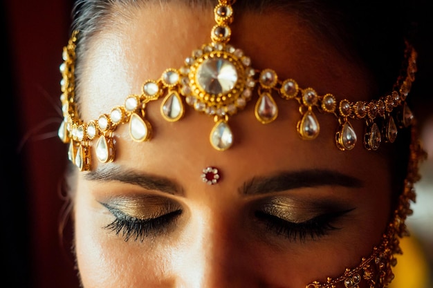 Portrait indian beautiful female in golden rich jewelery and tradition saree face closeup professional make-up wearing bindi on head .Muslim Woman face portrait with bindis maang tikka ,nath,nose Pin