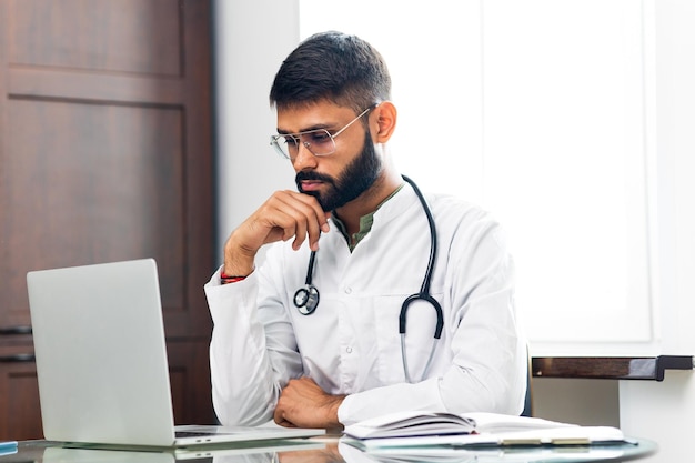 Portrait of indian man doctor talking to online patient on laptop online consultation