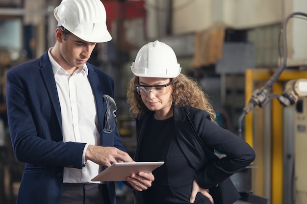 A portrait of an industrial man and woman engineer with tablet in a factory, working.