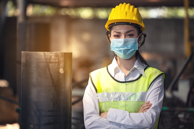 A portrait of an industrial woman engineer with mask standing in a factory.