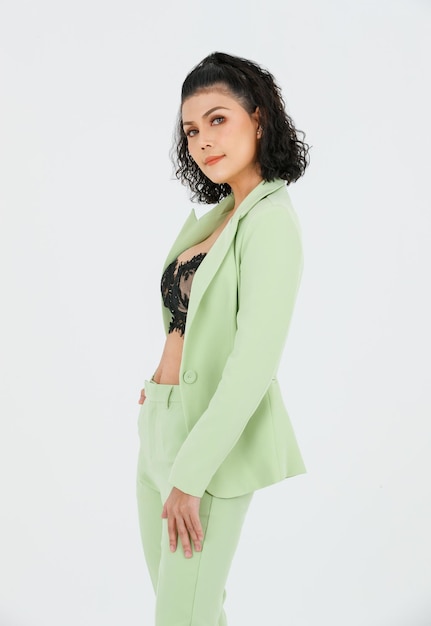 Portrait isolated cutout studio shot of Asian sexy curly hair fashion businesswoman in green suit with black lace lingerie crop top bra standing posing put hands in pants pockets on white background