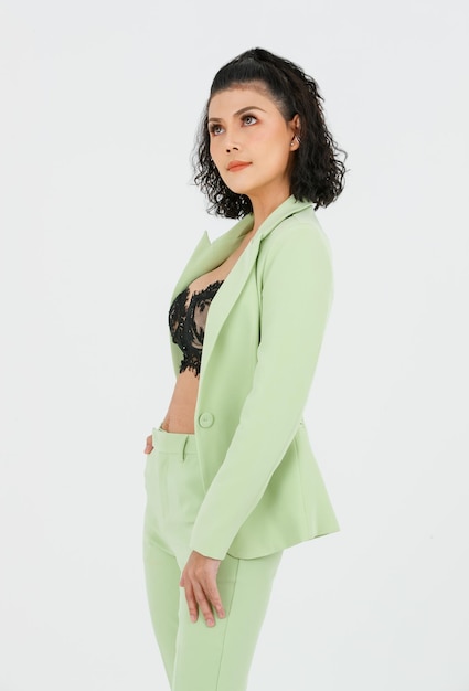 Portrait isolated cutout studio shot of Asian sexy curly hair fashion businesswoman in green suit with black lace lingerie crop top bra standing posing put hands in pants pockets on white background