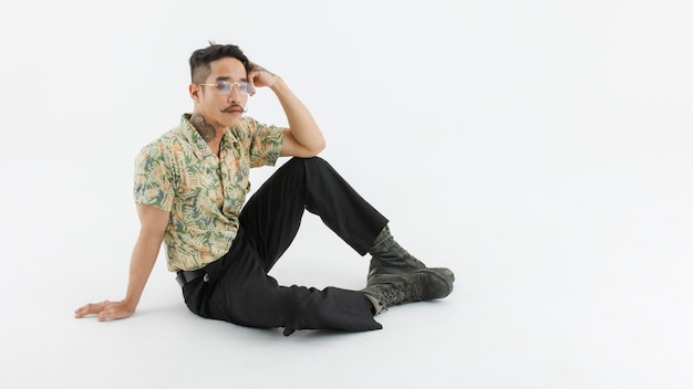 Portrait isolated cutout studio shot Asian vintage classic male fashion model with mustache neck arm tattoo wear glasses in casual classy outfit and leather boots sitting on floor on white background