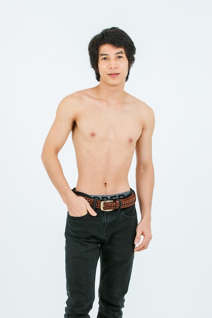 Portrait isolated cutout studio shot of Asian young handsome confident slim thin muscular shirtless teenager male model standing posing holding hand in denim jeans pants pocket on white background