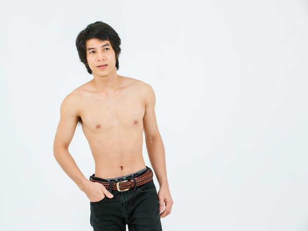 Portrait isolated cutout studio shot of Asian young handsome confident slim thin muscular shirtless teenager male model standing posing holding hand in denim jeans pants pocket on white background