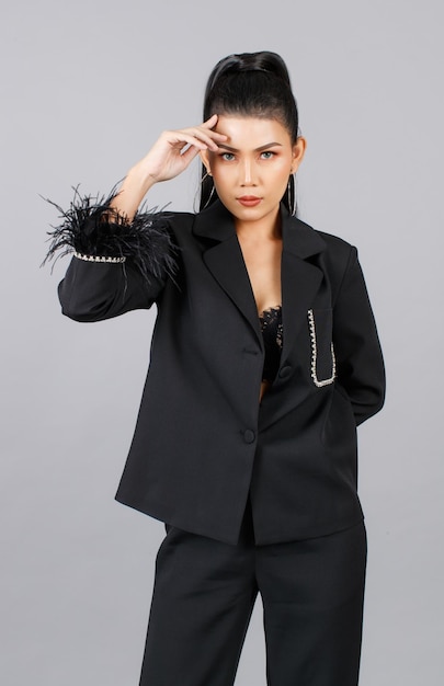 Portrait isolated cutout studio shot of Millennial Asian female elegant fashion model in black casual fashionable fur suit standing posing look at camera on gray background