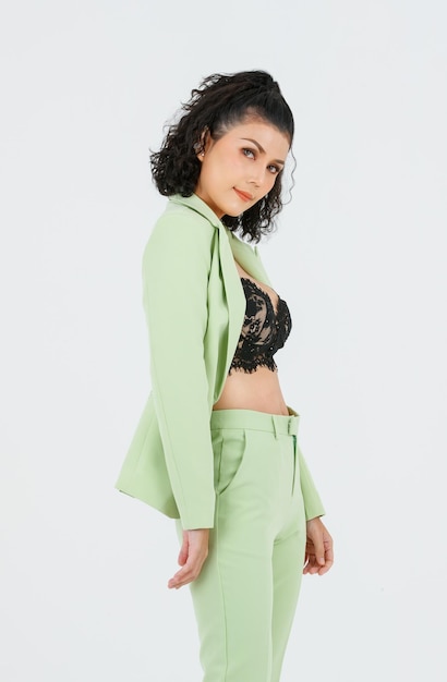 Portrait isolated studio full body shot of Asian young sexy curly hairstyle fashion model in green formal suit with black lace lingerie bra and high heels standing posing alone on white background