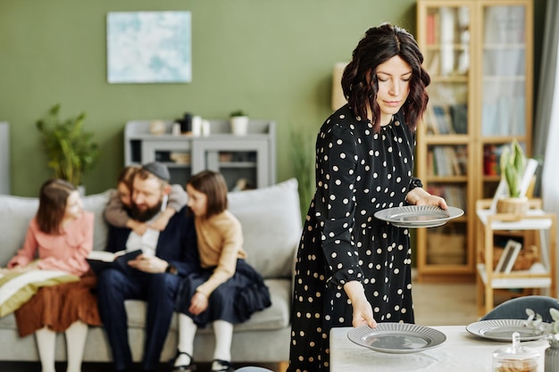 Portrait of jewish family at home with focus on young woman setting table with silverware copy space