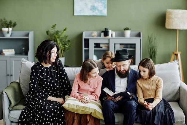 Portrait of jewish family with three children reading book together in modern home setting