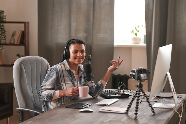 Portrait of joyful female influencer sitting at wooden table in front of desktop computer monitor ho