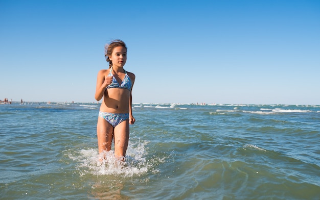 Portrait of a joyful little positive girl swimming in the sea on a sunny warm summer day. The concept of happy children having a rest at the sea. Advertising space