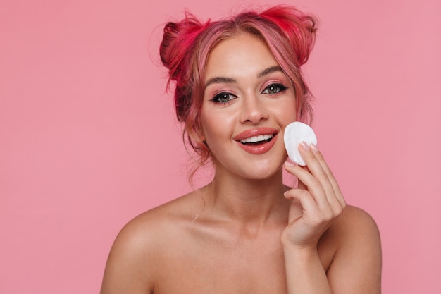 Portrait of joyful shirtless young woman cleaning her face with cotton pad