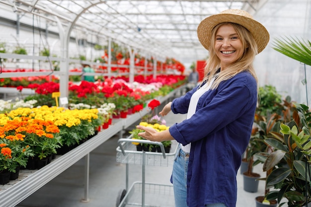 Portrait of a joyful woman pointing with her hands at a cart with flowers while shopping