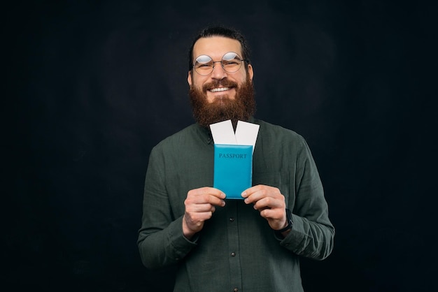 Portrait of joyful young man with beard holding passport at airplane tickets ready for vacation