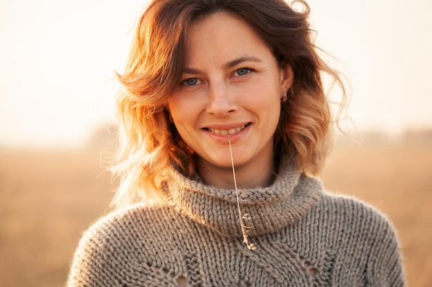 Portrait joyful young woman brunette in brown knit sweater made of natural wool and jeans holding a spike and smiles mysteriously and enjoy day on field stylish hipster woman