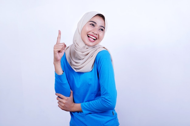 Portrait of Joyful young woman with blue t-shirt wearing hijab, feeling happy and pointing left side