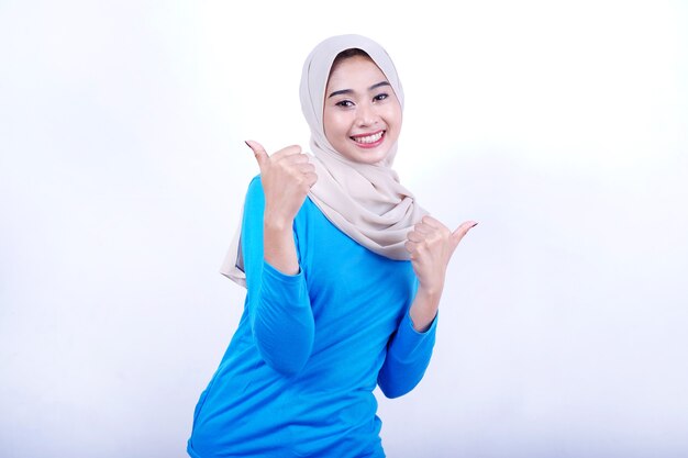 Portrait of Joyful young woman with blue t-shirt wearing hijab over white background giving a thumbs up gesture