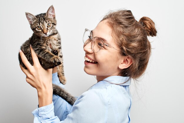 Portrait of a joyfully smiling young Asian Kazakh woman playing with a kitten on a white studio background