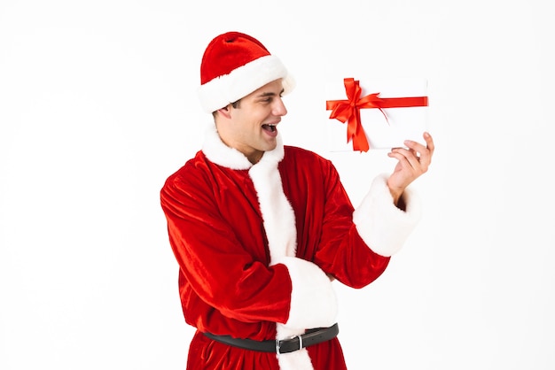 Portrait of joyous man 30s in santa claus costume and red hat holding present box