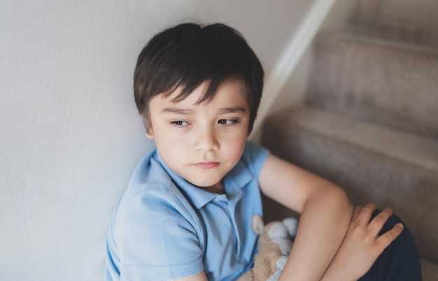 Portrait kid looking out deep in thought Lonely Child sitting on stairs carpet with thinking face Childhood and family concept Emotional child portrait indoor closeup face