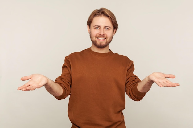 Portrait of kind-hearted generous bearded man in sweatshirt keeping hands up to embrace and support, smiling