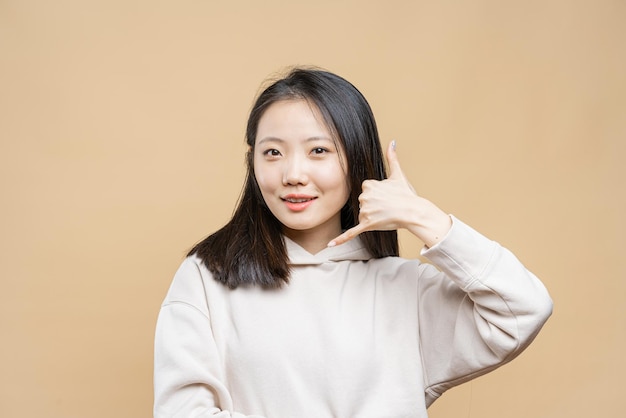 Portrait of a korean woman on a light brown background Asian girl makes phone gesture of calling