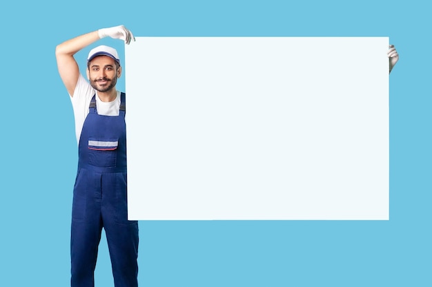 Photo portrait of labourer man in workwear and protective gloves raising big sheet poster template