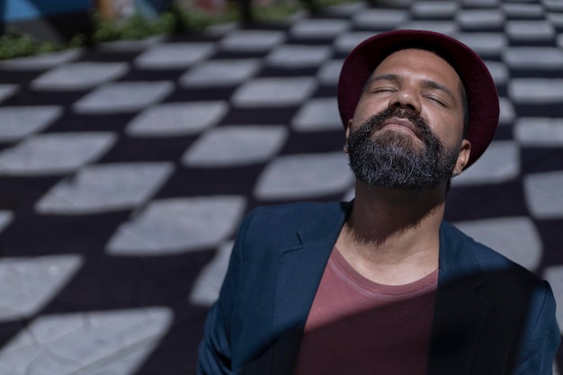 Portrait of Latin American bohemian man with closed eyes beard hat and jacket Background of shadows with rhombus shapes Concept Real people