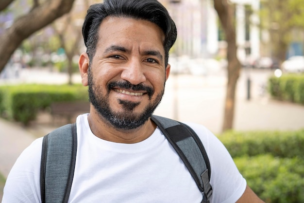 portrait of latin man with beard smiling at camera carrying a backpack