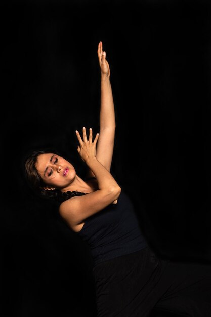 Portrait of a Latin woman posing isolated on black background looking down and stretching her arm up Female body expression concept