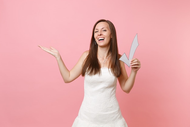 Portrait of laughing happy woman in white dress pointing hand aside, holding check mark,