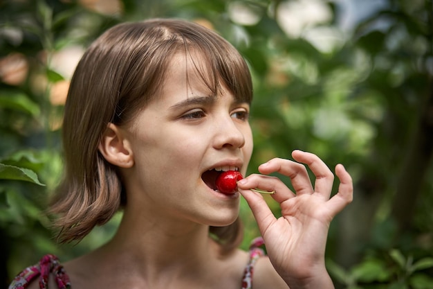 Portrait of laughing little girl eating cherries in the garden