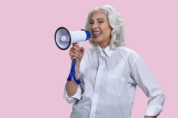 Portrait of laughing senior woman with megaphone isolated on pink background