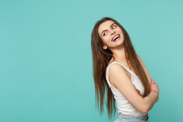 Portrait of laughing young woman in light casual clothes looking aside holding hands crossed isolated on blue turquoise wall background. People sincere emotions lifestyle concept. Mock up copy space.