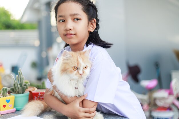 Portrait of a Little Asian girl in Thai student uniform is hugging her Persian cat with happiness, select focus shallow depth of field