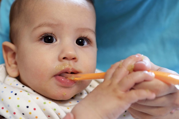 Portrait of little baby boy eating food Baby with a spoon in feeding chair Cute baby eating first meal