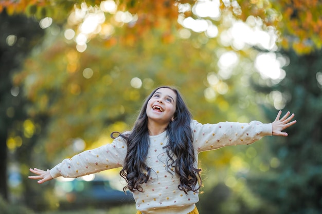 Portrait of a little beautiful girl of 9 years old with long dark hair in bright clothes Happy child in autumn park