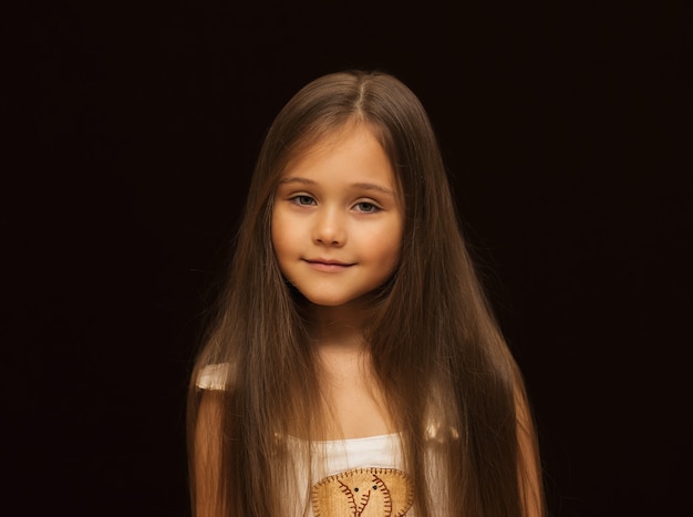 Portrait of a little beautiful girl with long hair against a dark background