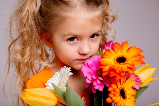 portrait of a little blonde girl with a bouquet of spring flowers on a light wall