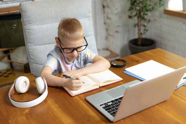 Portrait of little boy child in glasses studying at home looking on laptop working with teacher Online education